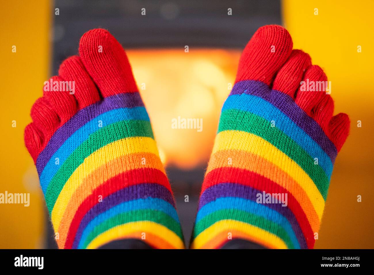 réchauffez vos pieds tout en portant des chaussettes strippy colorées avec un brûleur en bois illuminé en arrière-plan Banque D'Images