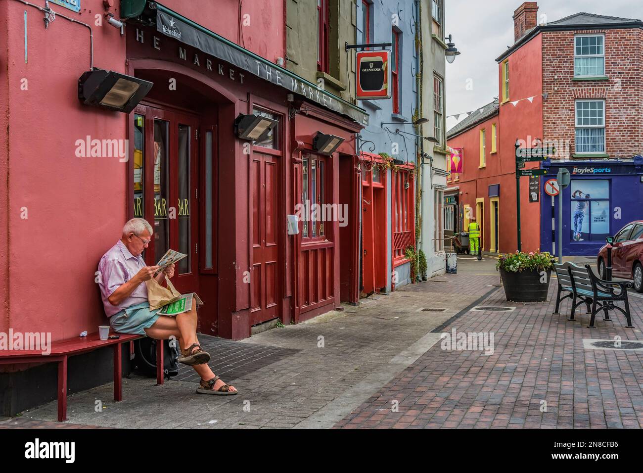 Homme lisant le journal du matin à côté du pub à la place du marché dans le centre-ville de Kinsale, co Cork, Irlande. Banque D'Images