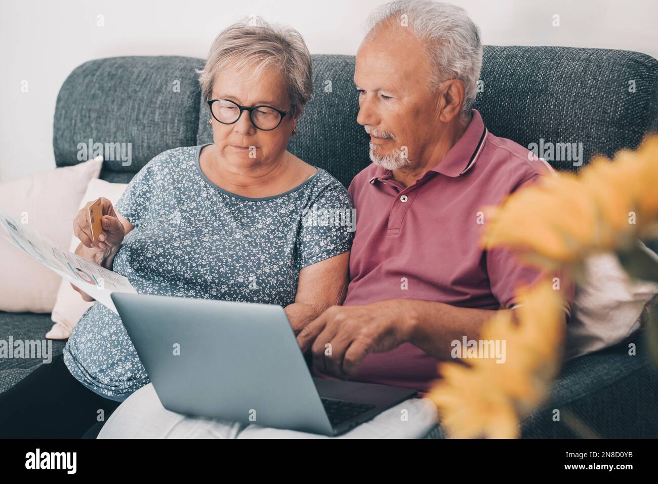 Un vieux couple senior à la maison payant des factures en ligne avec l'application Web Banking et vérifier les montants sur les documents. La vie réelle des technologies âgées et modernes. Banque D'Images