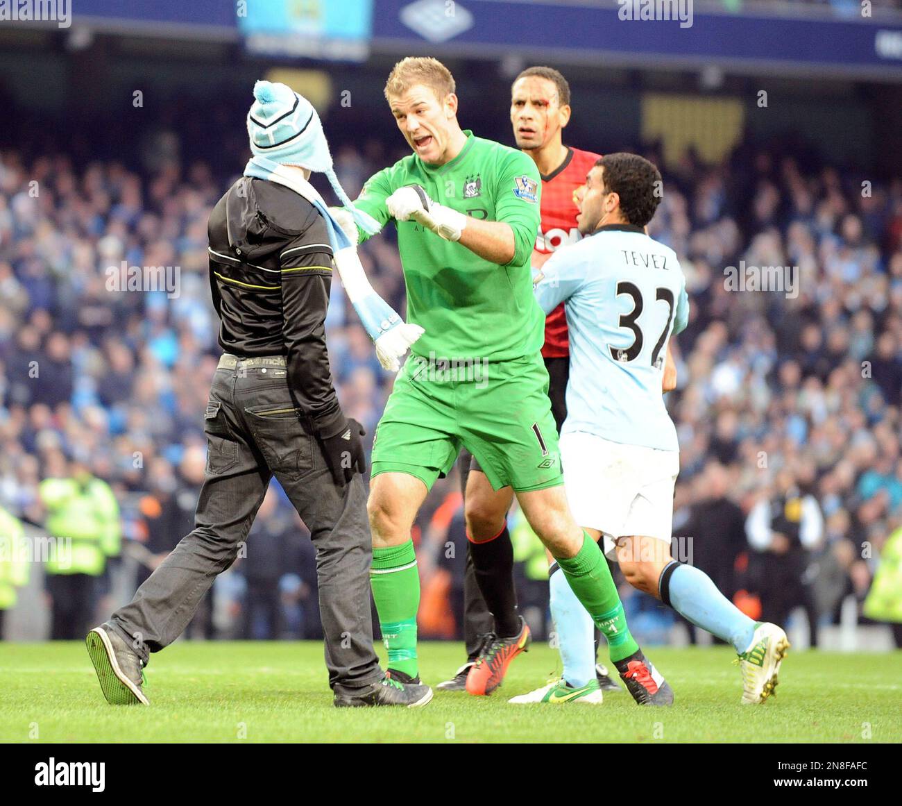 Manchester City's Joe Hart, second left, stops a fan, left, who walks onto the pitch to confront Manchester United's Rio Ferdinand,background,with Manchester City's Carlos Tevez hold Ferdinand back, during their Premier League soccer match at the Etihad Stadium in Manchester, England, Sunday Dec. 9, 2012. (AP Photo/Clint Hughes) Banque D'Images