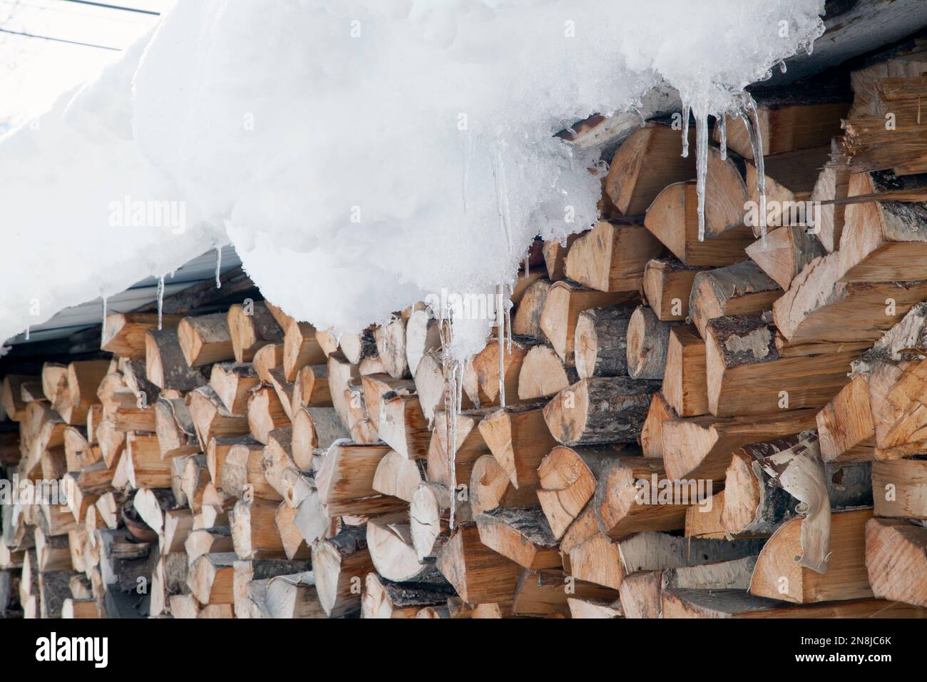 Bois coupé et entreposé pour l'hiver dehors sous un toit enneigé, Jarrier, Maurienne, Savoie, France Banque D'Images