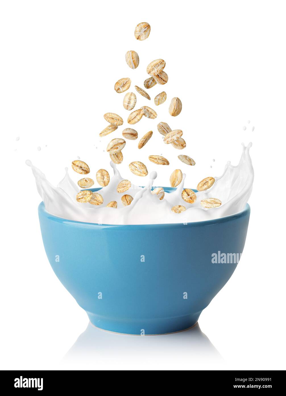 flocons d'avoine tombant dans un bol bleu avec éclaboussures de lait isolées sur du blanc Banque D'Images