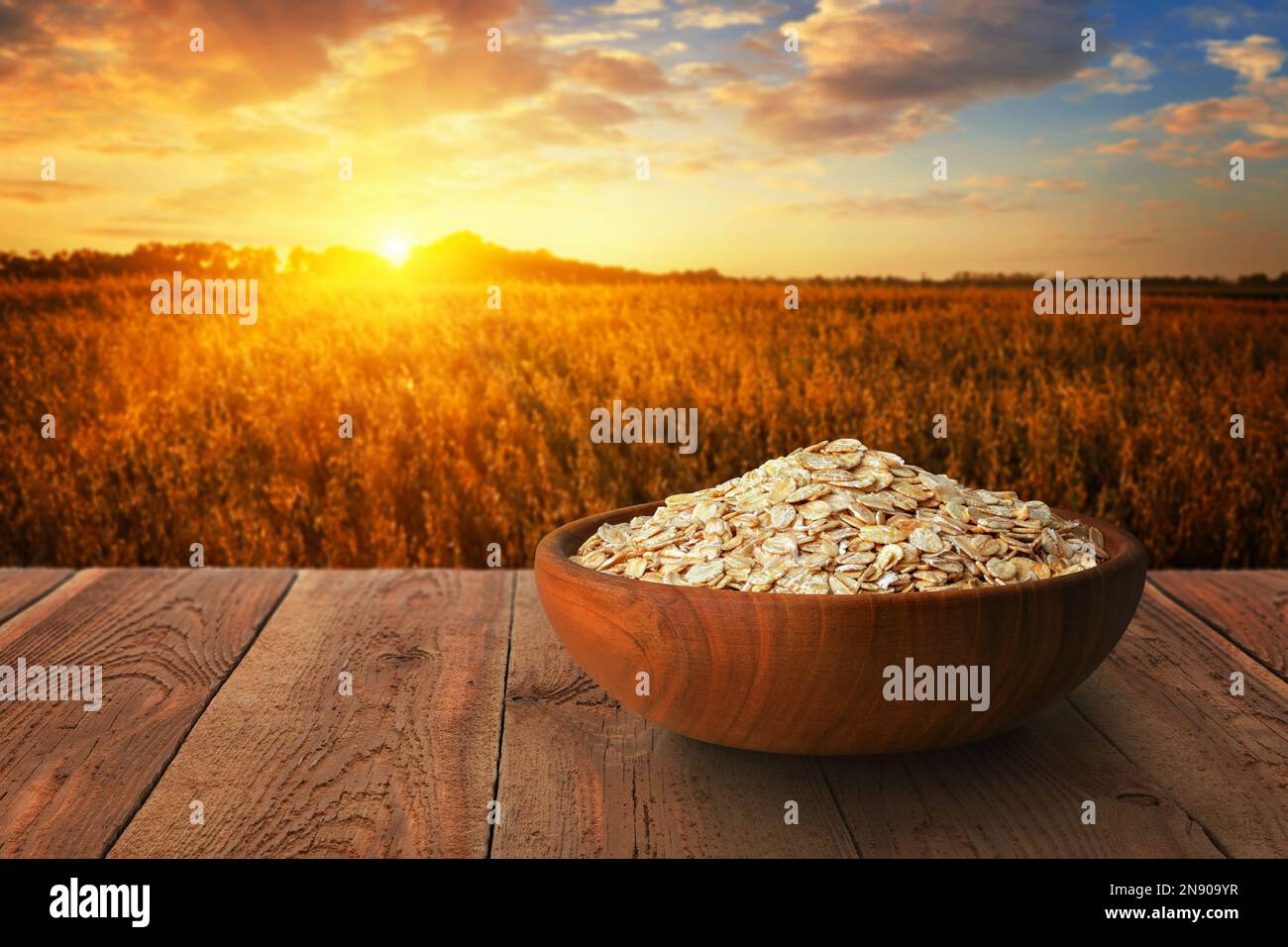 flocons d'avoine dans un bol sur la table, champ de céréales mûres sur le coucher du soleil comme arrière-plan Banque D'Images