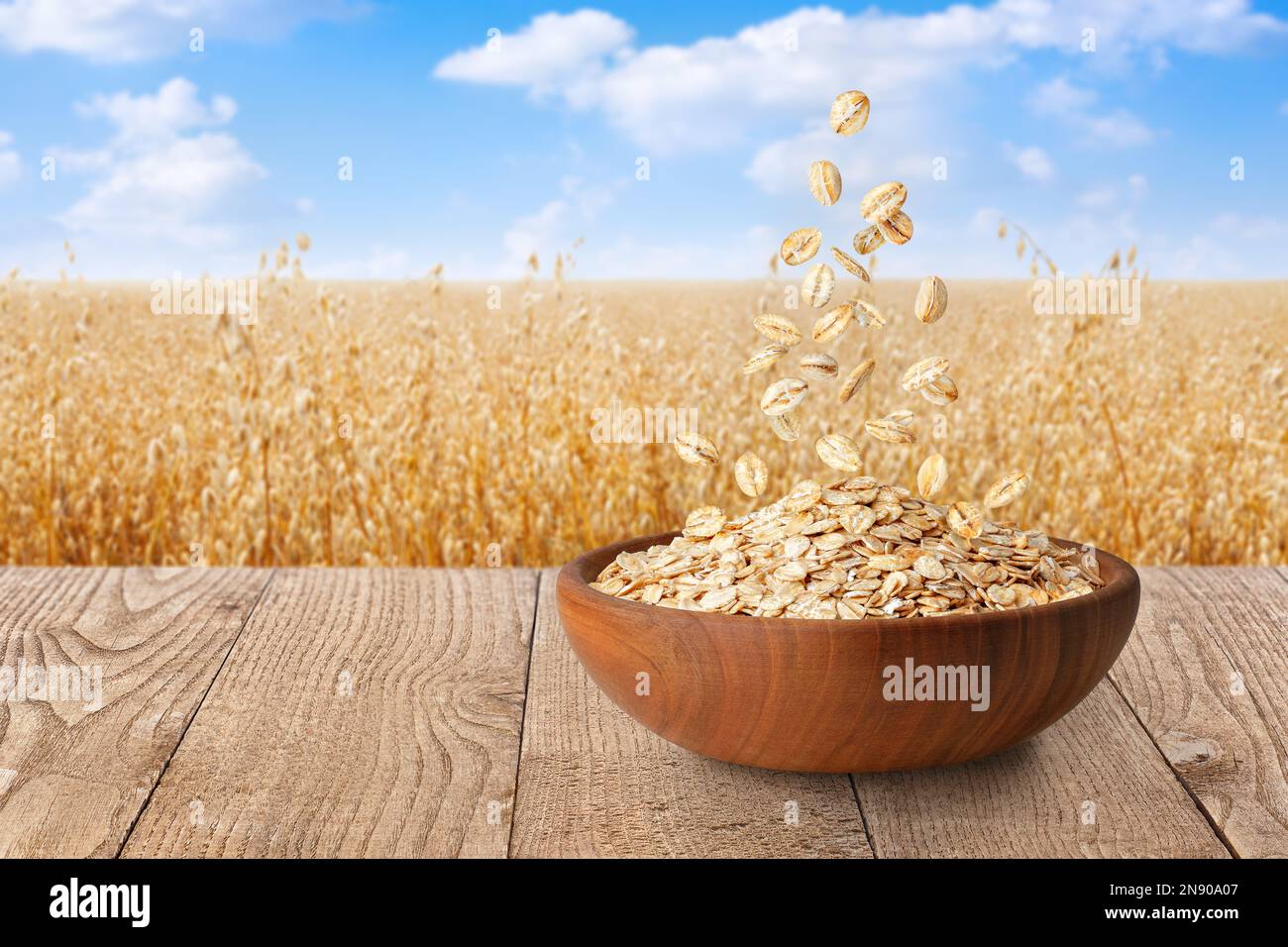 flocons d'avoine tombant dans un bol sur la table avec champ de céréales mûres sur le fond Banque D'Images