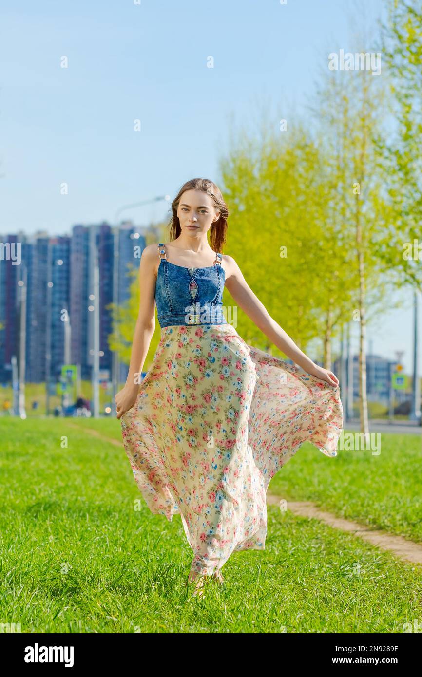 Belle jeune femme heureuse robe longue fleur volant ses cheveux en  profitant de temps libre à l'extérieur dans la ville contre les arbres de  toile de fond et le ciel bleu. Beauté