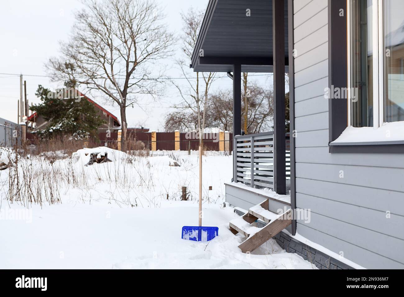 Cour enneigée près de la maison avec une pelle coincée dans la neige, déneigement du site Banque D'Images