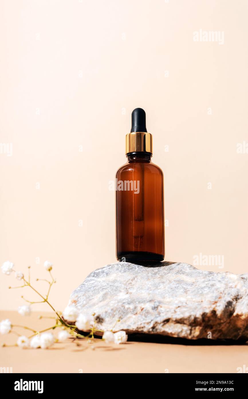 Bouteille de sérum en verre ambré sur pierre naturelle avec fleurs de sophila. Arrière-plan beige neutre. Beauté, concept de soin de la peau. Banque D'Images
