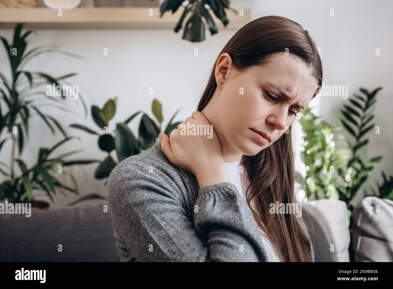 Objectif sélectif de la jeune femme malsaine ayant des douleurs au cou assis sur un canapé à la maison. La fille bouleversée a la douleur des muscles. Ostéochondrose cervicale, fatiguée Banque D'Images