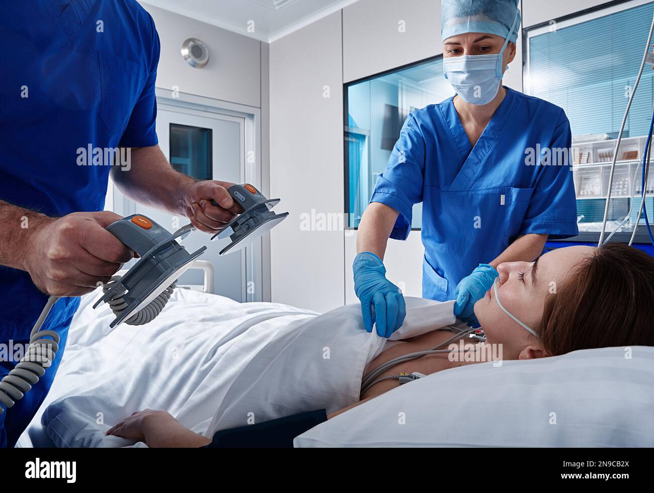 équipe médicale réalisant une réanimation avec défibrillateur sur une patiente inconsciente allongée dans un service hospitalier. RCP en USI Banque D'Images