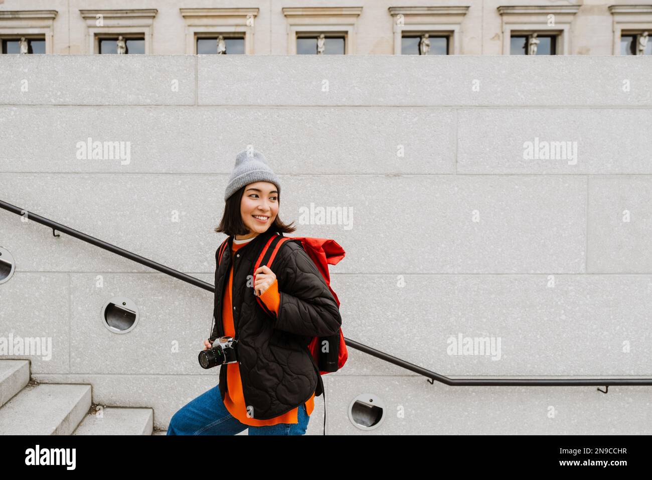 Belle gaie jeune femme asiatique avec sac à dos et appareil photo grimper les escaliers dans la rue de la ville Banque D'Images