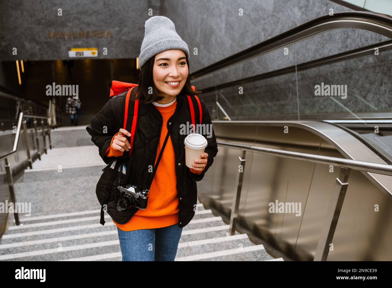Belle jeune femme asiatique souriante dans des vêtements chauds boire un café à emporter tout en montant les escaliers à l'extérieur Banque D'Images