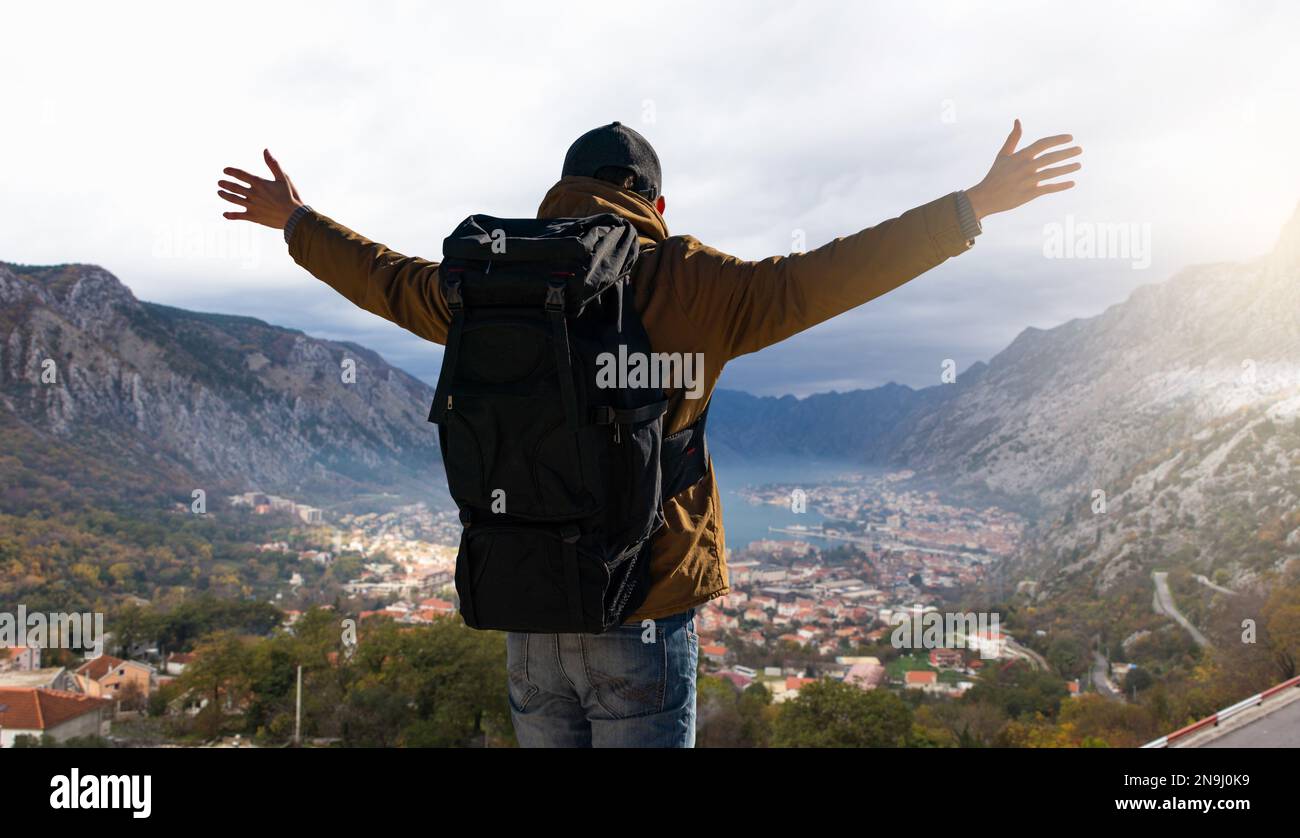 Un voyageur avec un sac à dos se tient au sommet de la montagne et tient ses mains sur les côtés Banque D'Images