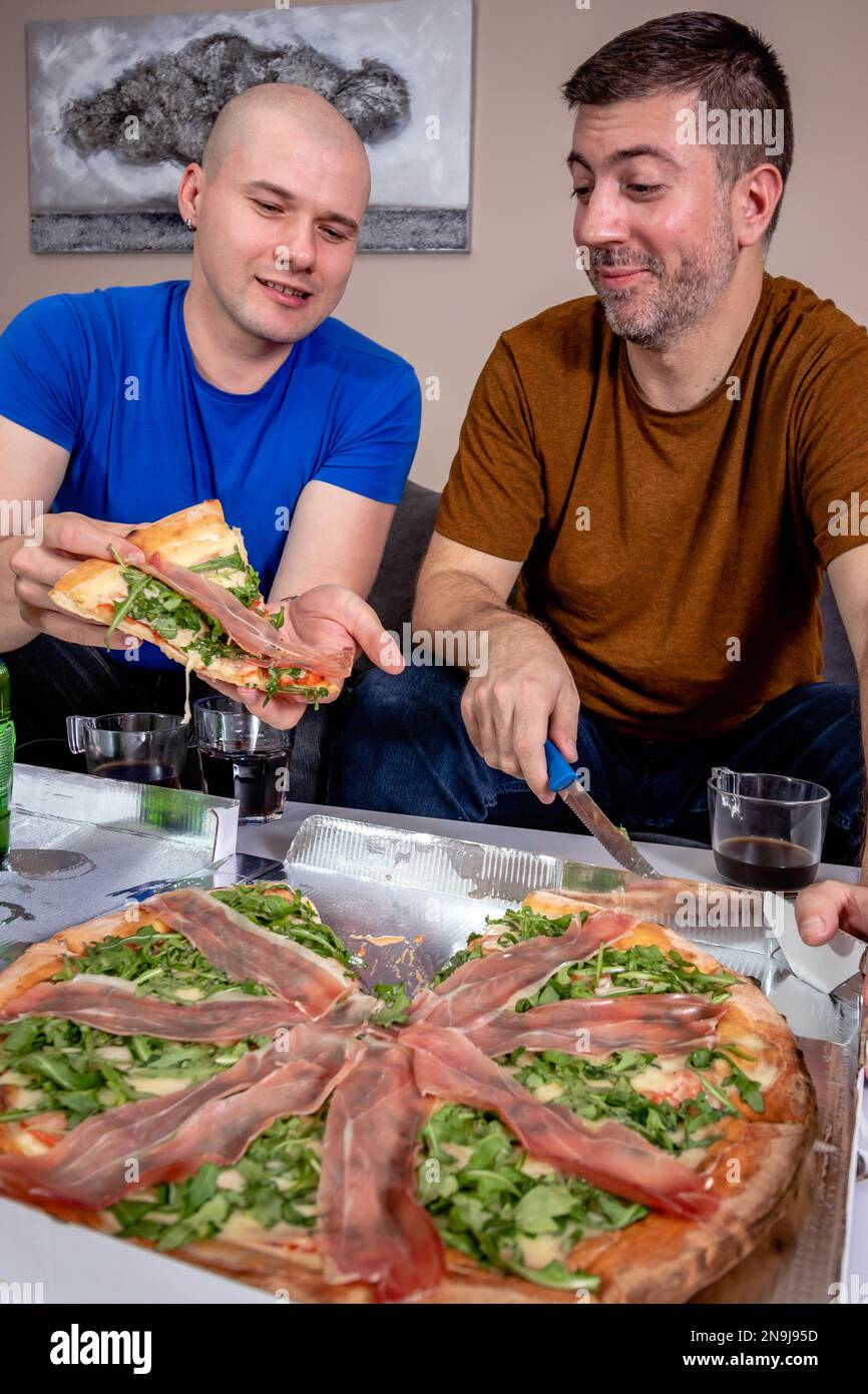 Deux amis qui mangent de la pizza. S'amuser et faire la fête à la maison. Banque D'Images