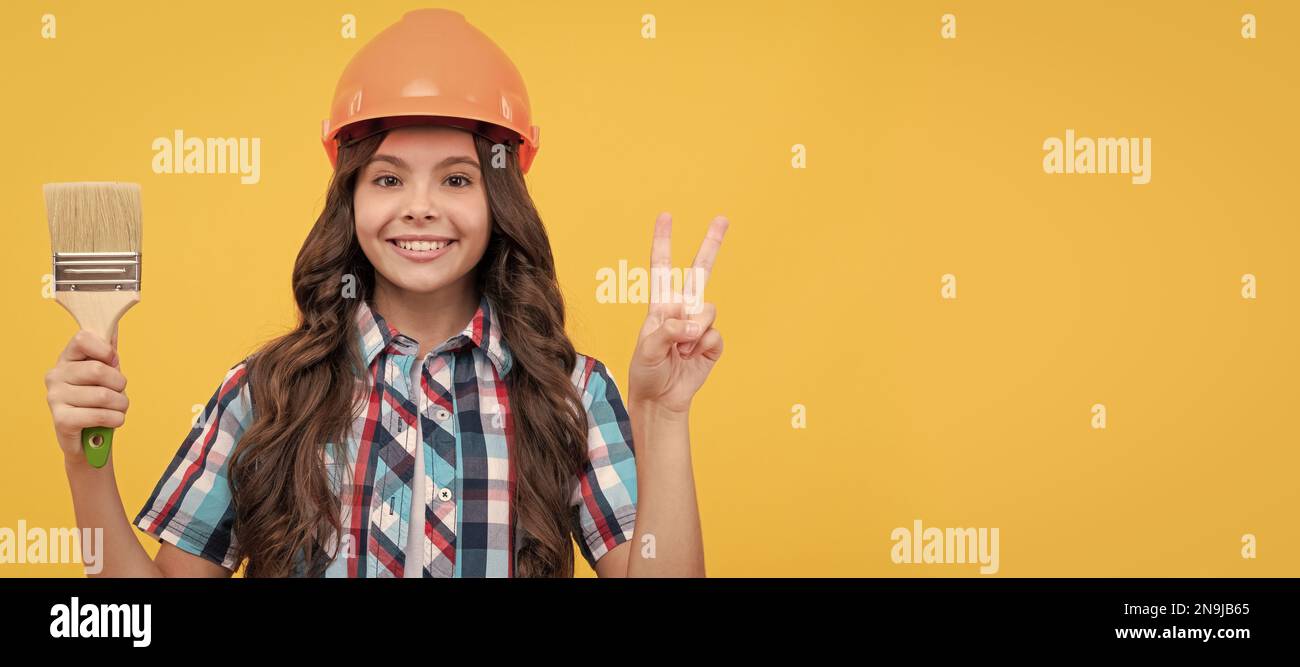 Rénovation enfant, bonne fille de l'adolescence dans la construction casque tenir la peinture brosse montrer la paix geste, la décoration. Affiche horizontale pour le constructeur d'enfants Banque D'Images