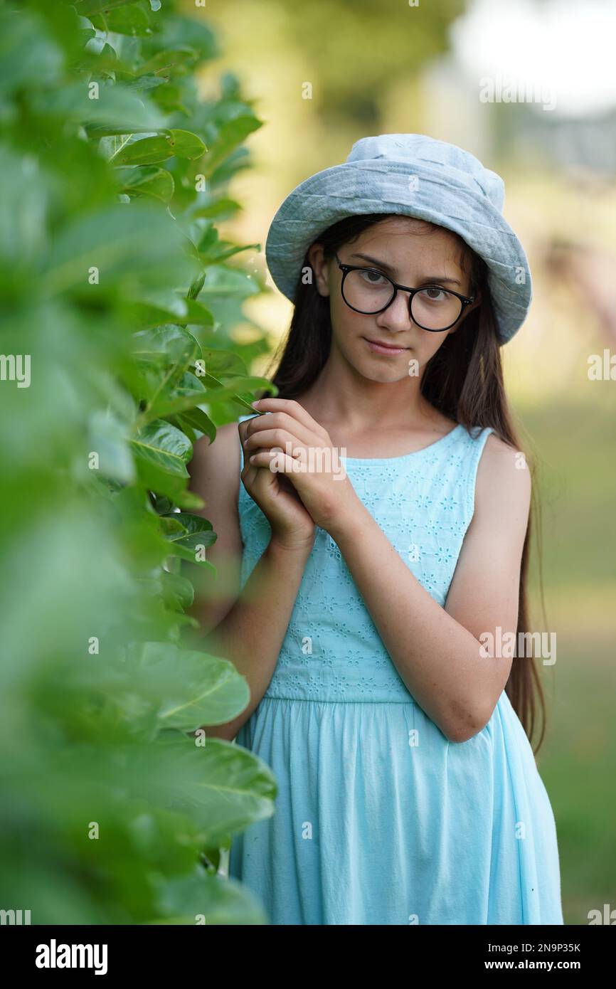 Une jolie petite fille en lunettes et une robe simple touche délicatement  le feuillage vert. Mise au point sélective Photo Stock - Alamy