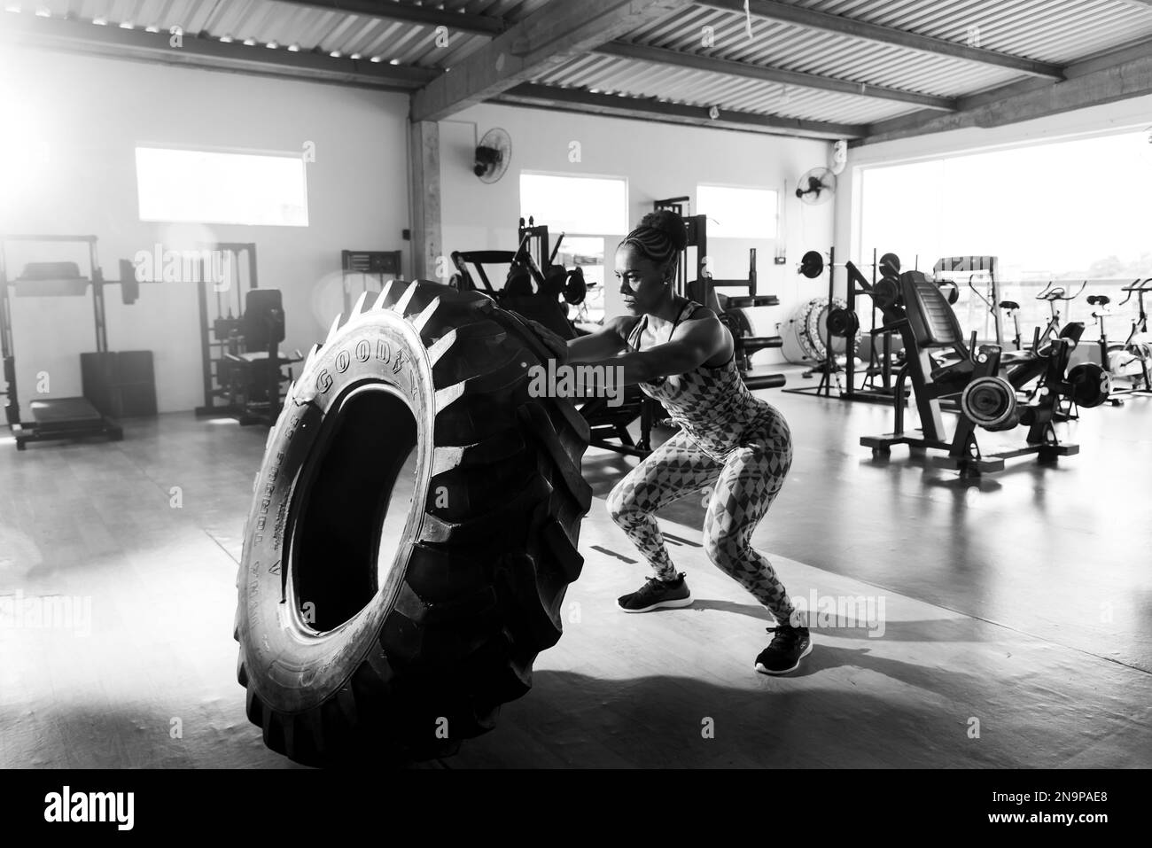 Jeune femme robuste qui soulève un pneu pour la musculation. Exercice de remise en forme dans le studio. Banque D'Images