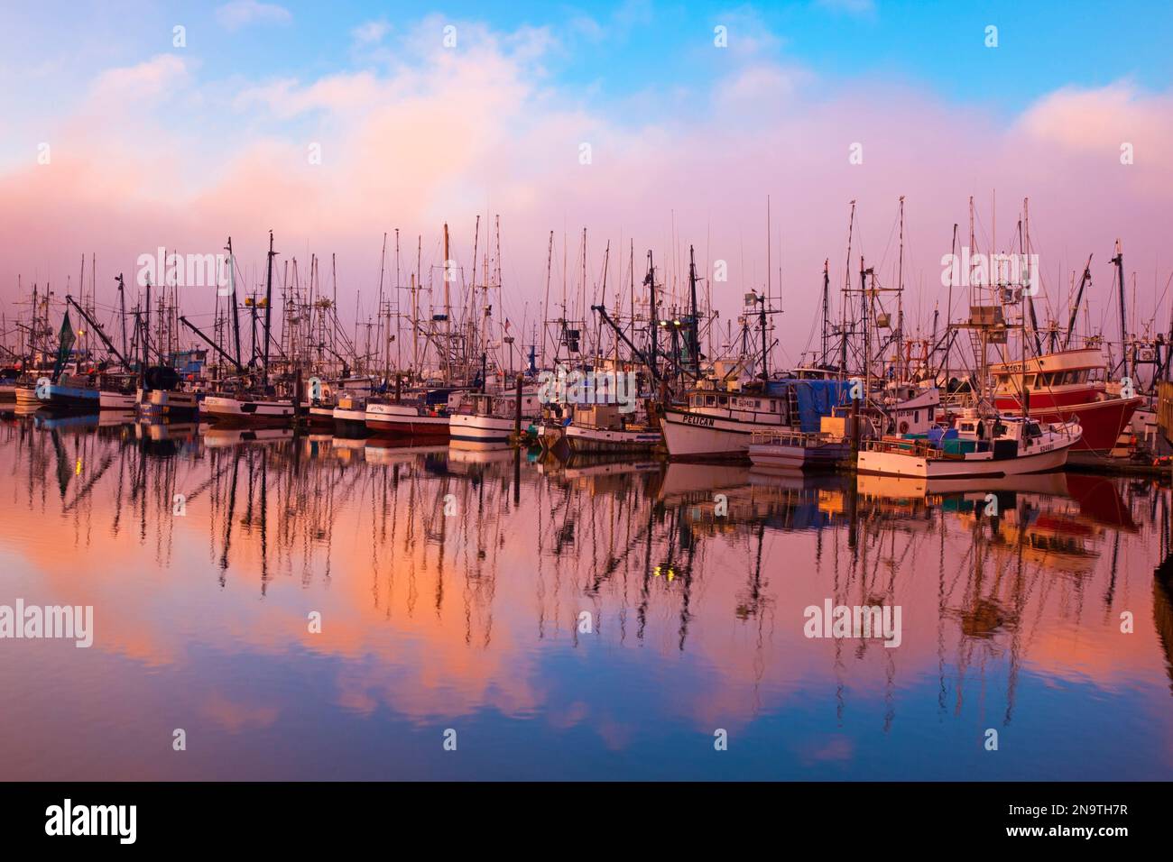 La lumière du lever du soleil à travers le brouillard matinal et les bateaux de pêche se reflète en image miroir dans l'eau dans le port de Newport sur la côte de l'Oregon Banque D'Images