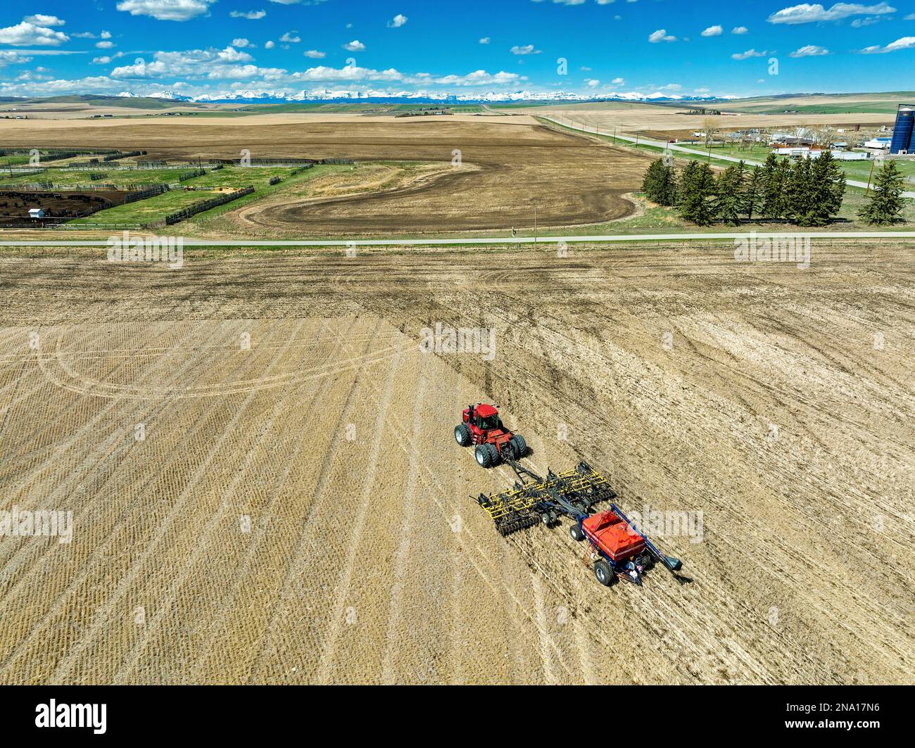 Vue aérienne du tracteur et du semoir, champ d'ensemencement avec ciel bleu, nuages et montagnes en arrière-plan, à l'ouest de High River, Alberta ; Alberta, Canada Banque D'Images