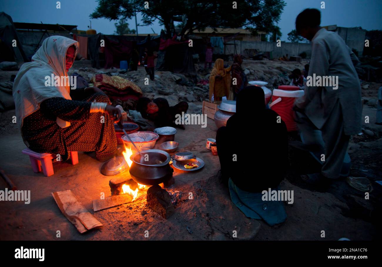 A Pakistani gypsy woman surrounded by her family cooks food in the open after authorities bulldozed their house due to illegal occupancy in Rawalpindi, Pakistan on Monday, April 9, 2012. (AP Photo/B.K. Bangash) Banque D'Images