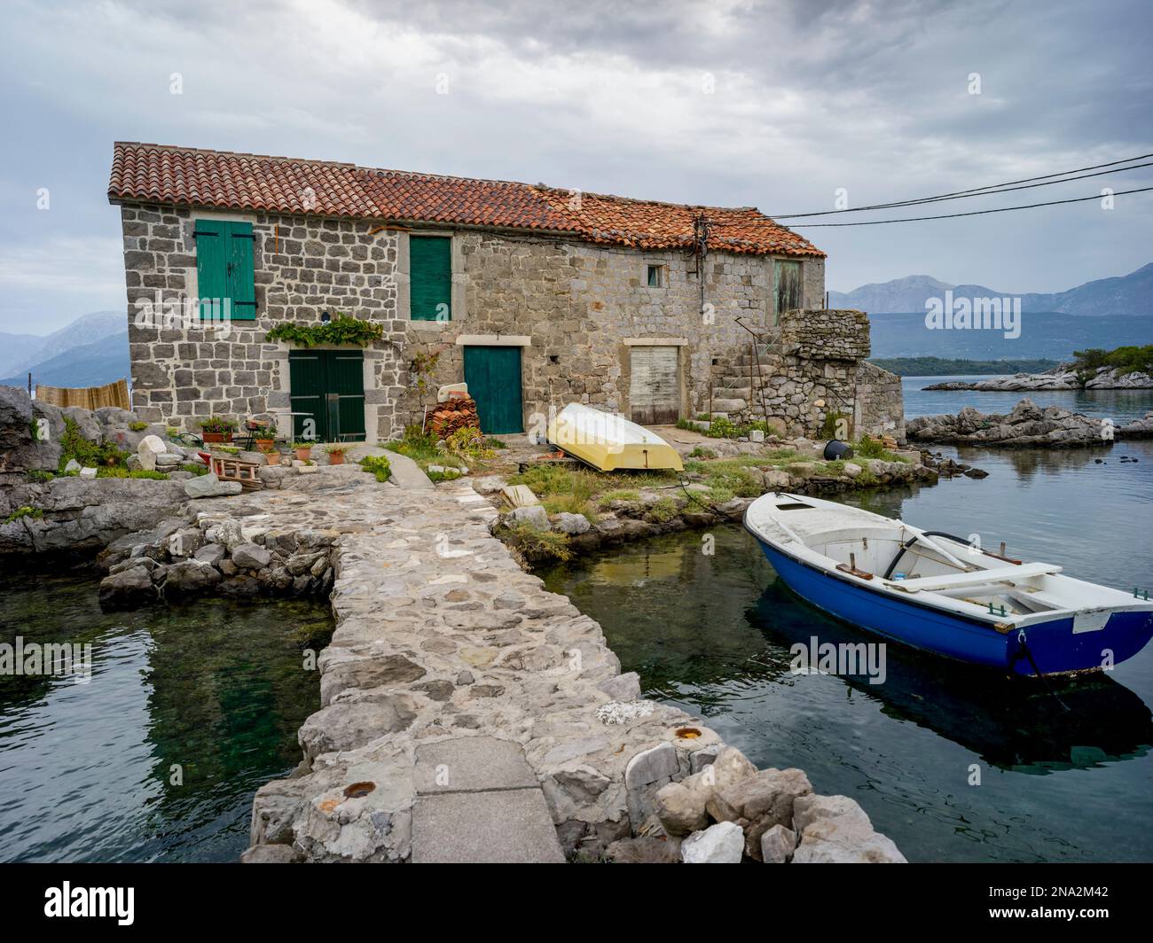 Un petit bateau s'amarre à l'extérieur d'une maison en pierre sur la baie de Kotor; Bjelila, Opstina Tivat, Monténégro Banque D'Images
