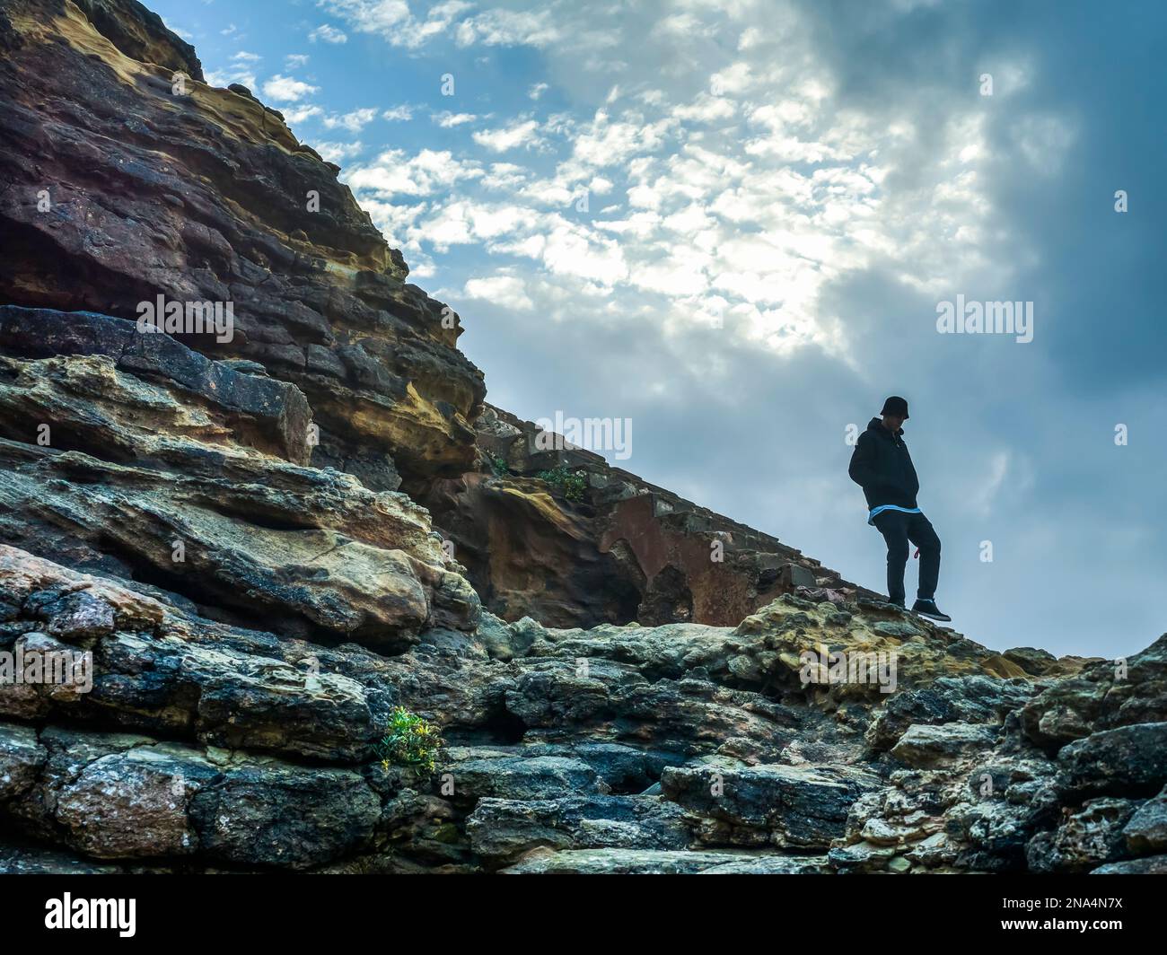 Jeune homme marchant sur un terrain rocheux et accidenté le long de la plage de Nazaré; Nazaré, district de Leiria, Portugal Banque D'Images