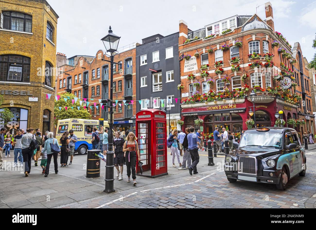 Scène de rue animée et vie de la ville sur un coin de rue avec cabine téléphonique rouge ; Londres, Angleterre Banque D'Images