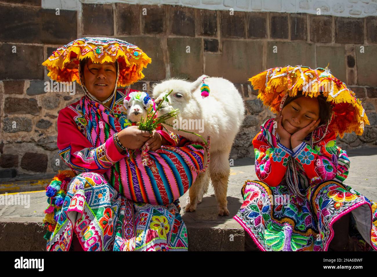 Mère péruvienne et jeune fille en robes et chapeaux colorés traditionnels posant avec deux bébés alpaga ; Cusco, Cusco, Pérou Banque D'Images