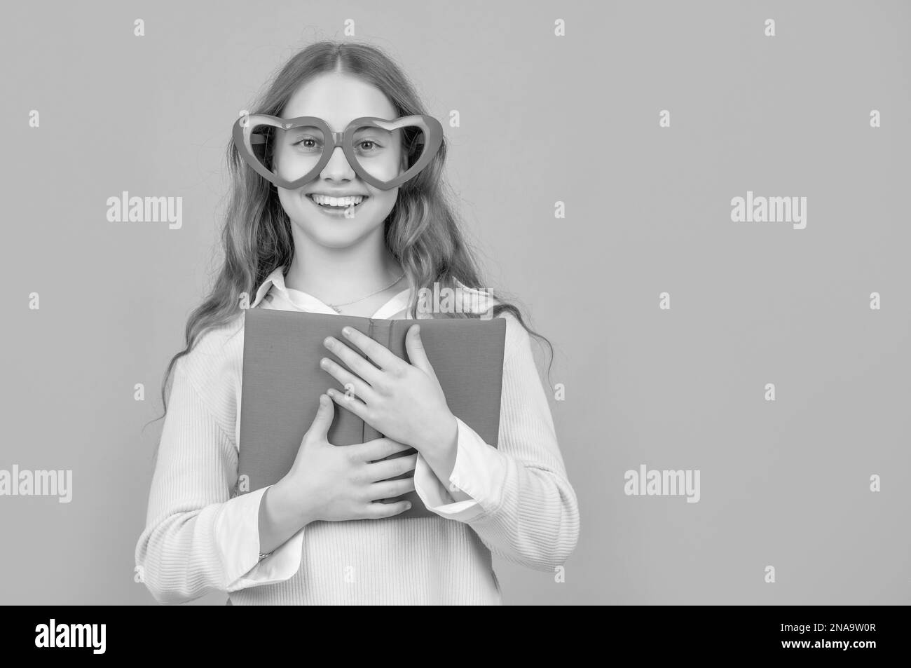 Joyeux écolier tenant un livre d'école portant de grandes lunettes en forme de coeur amusant fond bleu Banque D'Images