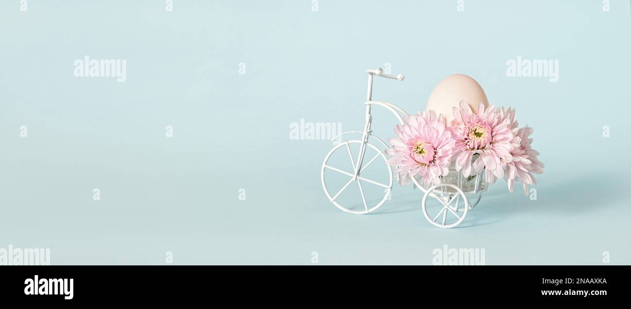 Petite figurine de tricycle blanc avec fleurs de chrysanthème rose et œuf de poulet unique, concept de Pâques avec espace de copie Banque D'Images