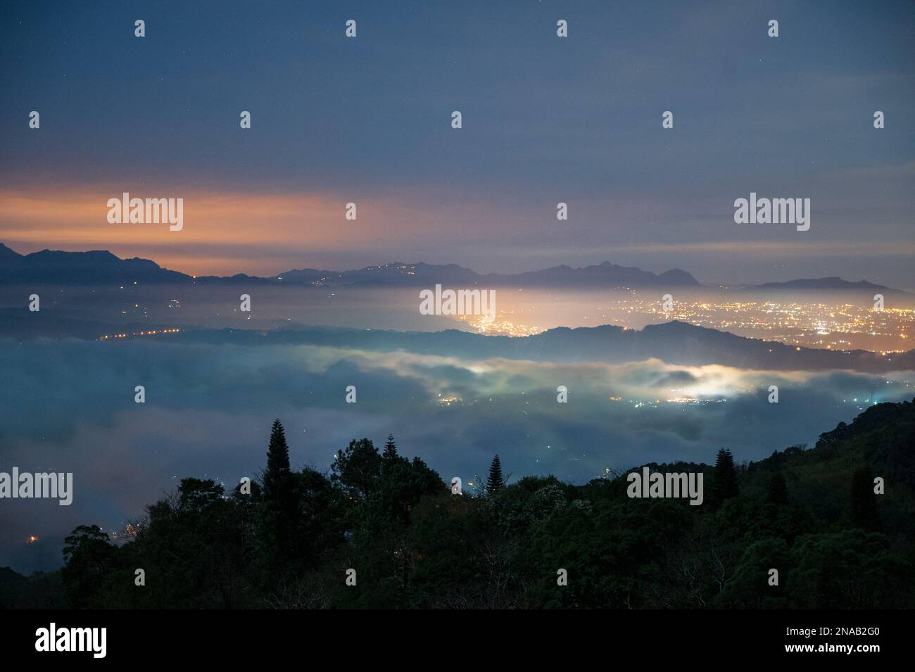 Vue nocturne des lumières de la ville dans la vallée. Spectaculaire cascade de nuages dans le ciel. La mer des nuages paysage. Canton de Dahu, comté de Miaoli, Taïwan Banque D'Images