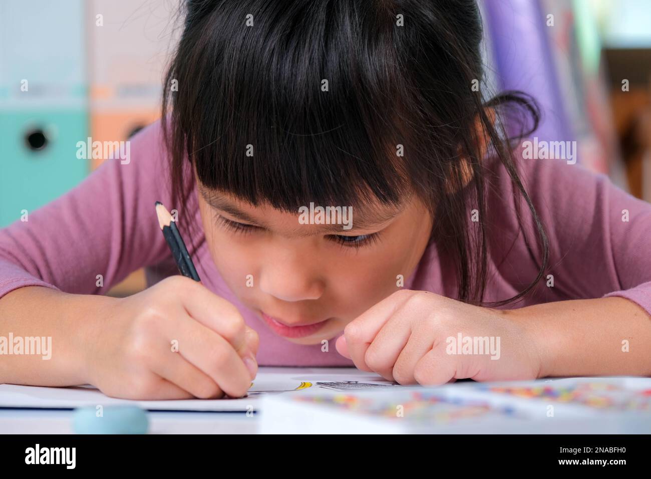 Bonne petite fille dessin avec des crayons de couleur sur papier assis à une table dans sa chambre à la maison. La créativité et le développement de compétences moteur fines. Banque D'Images