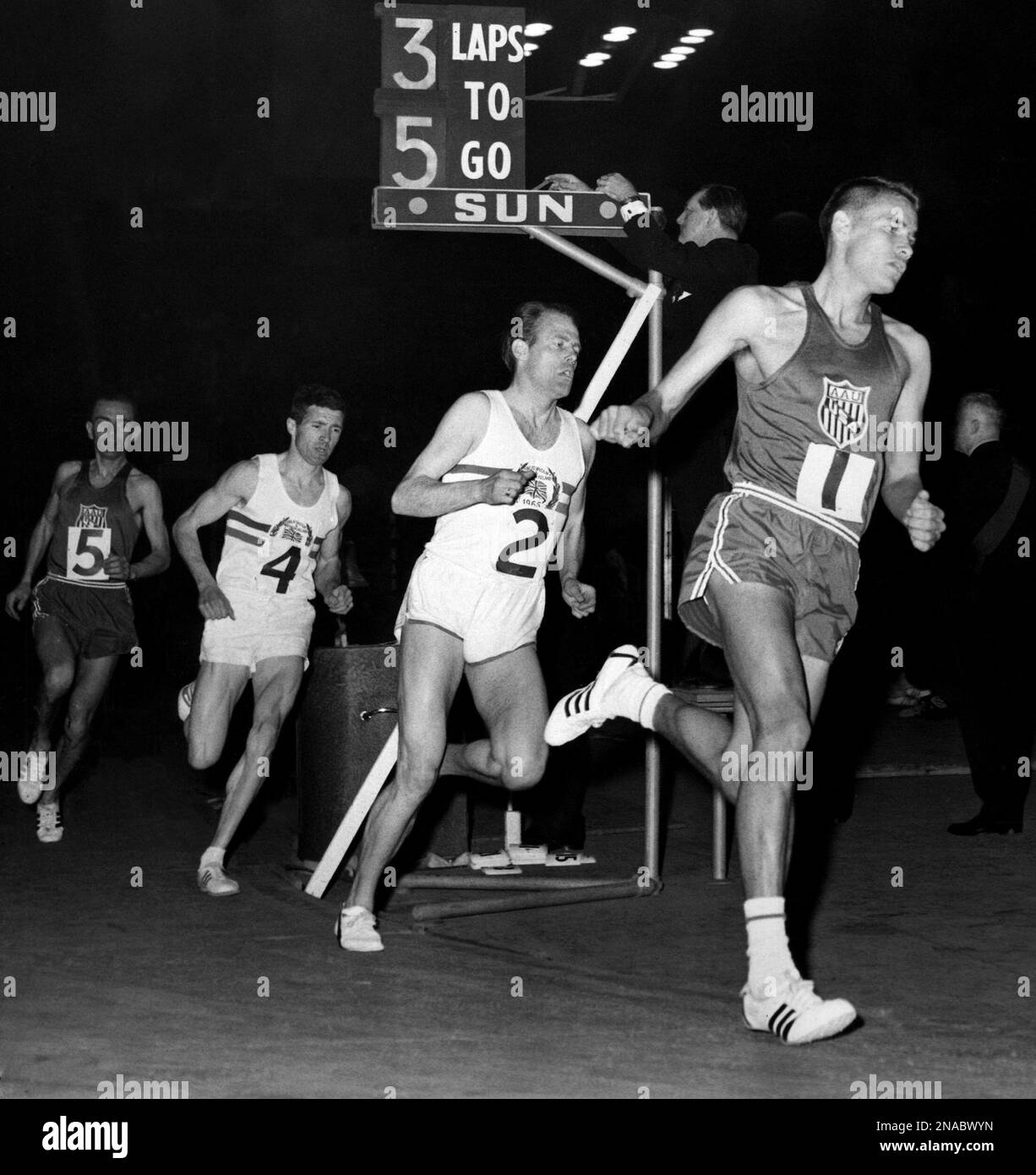 Billy Mills of the United Sates (1), the eventual winner, is ahead of the field in the three-mile event as the runners lap the track during the Great Britain vs. United States two-day indoor athletics match at Wembley Stadium, near London, April 3, 1965. Others are Britain's Derek Ibbotson (2), third; Britain's John Cooke (4), second, and Frank Pflaging of the United States (5), fourth. Mills' time of 13 minutes, 36.8 seconds was a new U.K. all-comers' record. (AP Photo/Rider-Rider) Banque D'Images