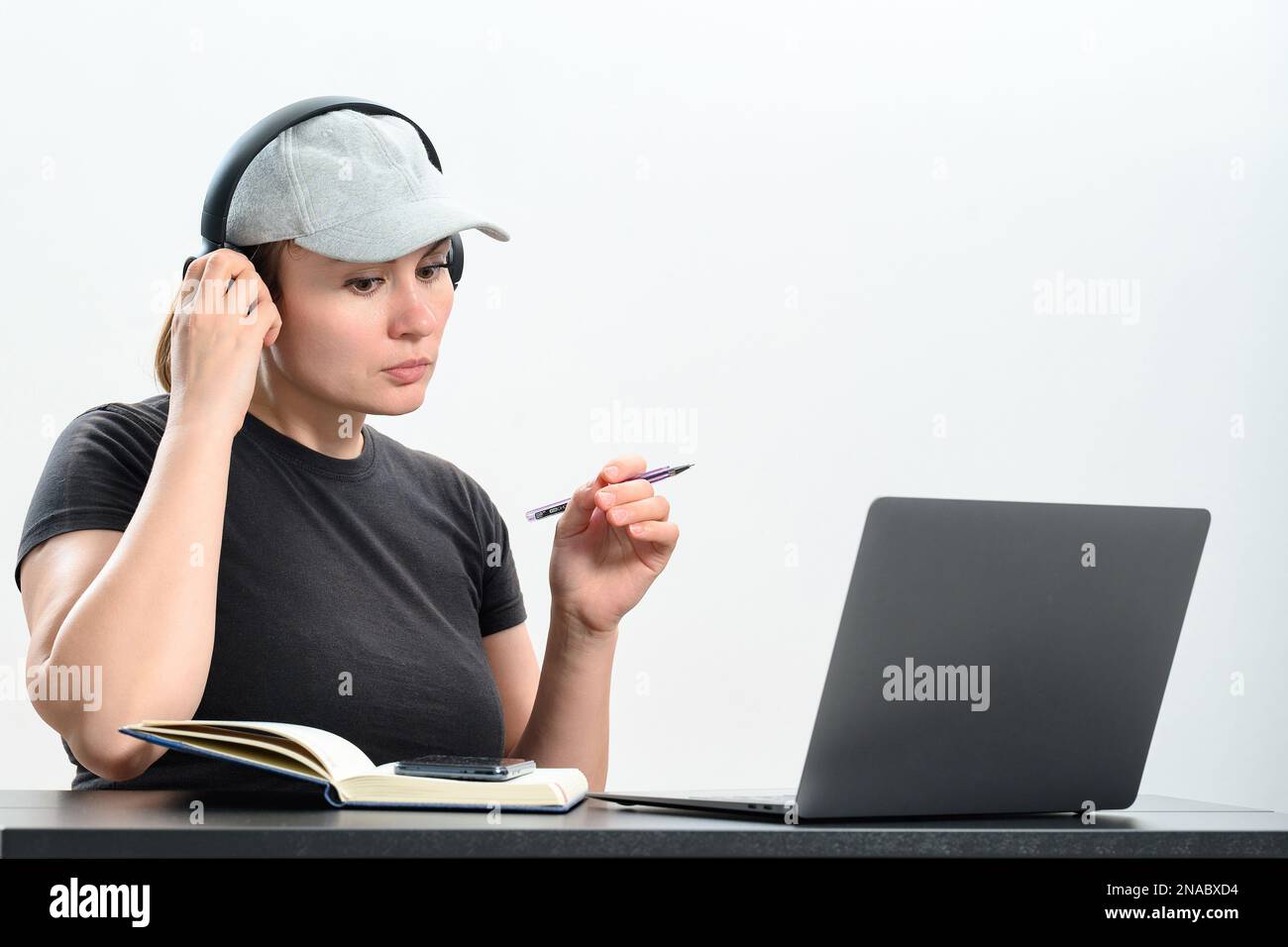 Une jeune femme active dans un casque qui travaille sur un ordinateur portable, qui fait des appels vidéo et prend des notes sur un ordinateur portable, travaille et étudie en ligne. Banque D'Images