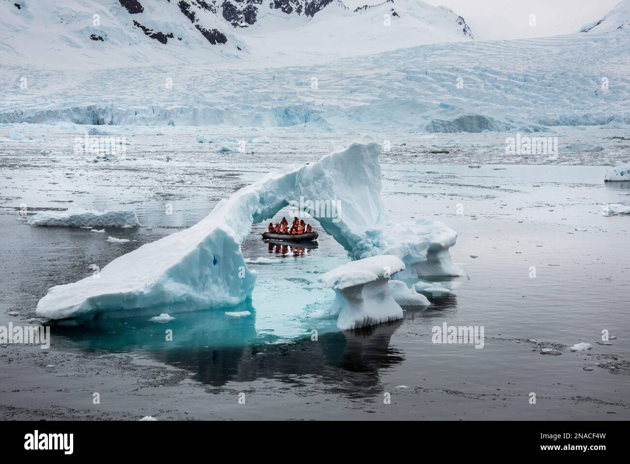Les visiteurs de l'anse Cierva en Antarctique, qui fait partie de la Terre Graham sur la péninsule antarctique, regardent un fragment d'iceberg en forme d'arc Banque D'Images