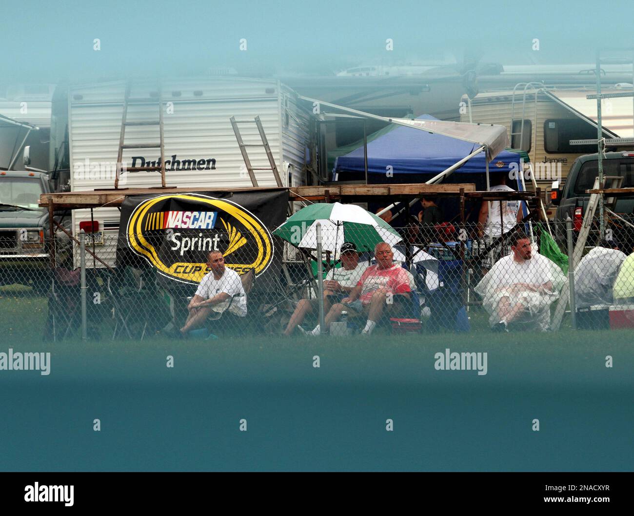 Seen through a blue safety barrier, fans wait in the rain for the start of the NASCAR Heluva Good! Sour Cream Dips at The Glen auto race Sunday, Aug. 14, 2011, at Watkins Glen International in Watkins Glen, N.Y. The race was postponed. (AP Photo/John Zeedick) Banque D'Images