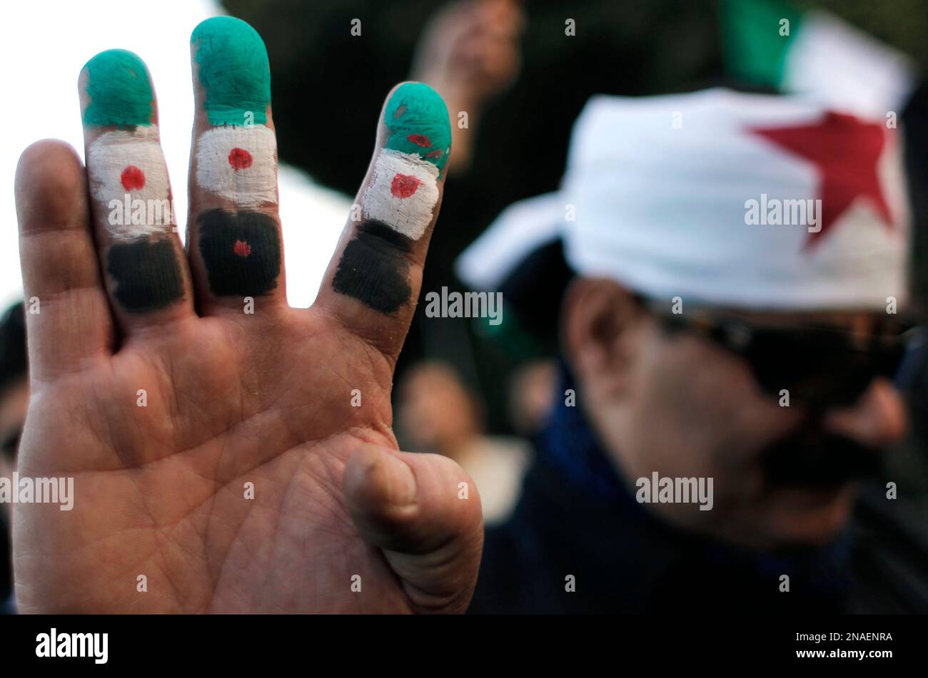 An anti-Syrian regime protester holds up his fingers painted in revolutionary flag colors during a protest outside the Arab League headquarters in Cairo, Egypt Sunday, Jan. 22, 2012. Arab League foreign ministers, meeting in Cairo, extended the much-criticized observers mission for another month, officials from the 22-member organization said. The League decided to add more observers and provide them with additional resources, the officials said. (AP Photo/Nasser Nasser) Banque D'Images