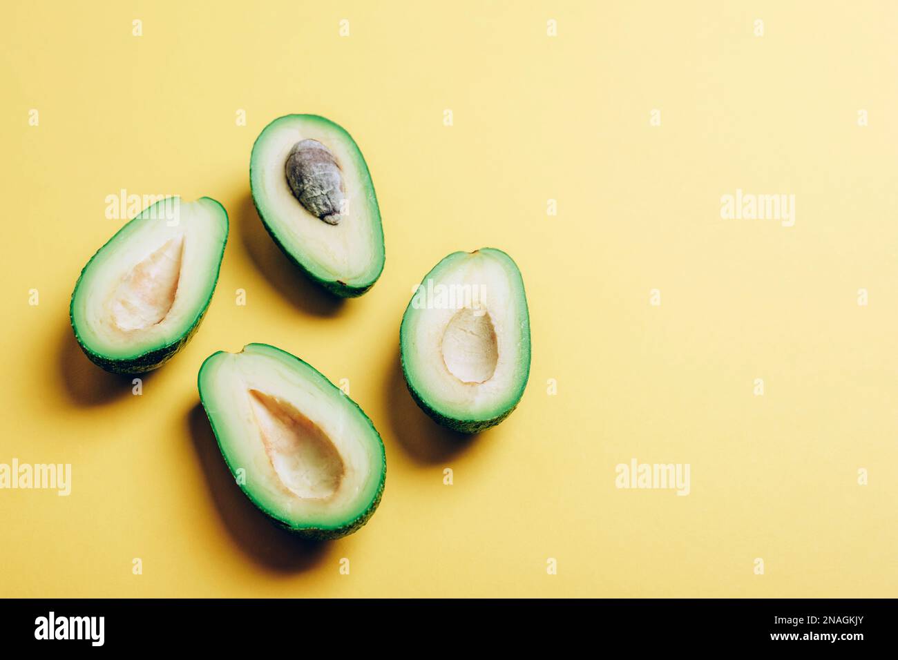 Moitiés d'avocat sur fond jaune avec des ombres nettes. Concept alimentaire végétalien sain. Vue de dessus, espace de copie. Banque D'Images