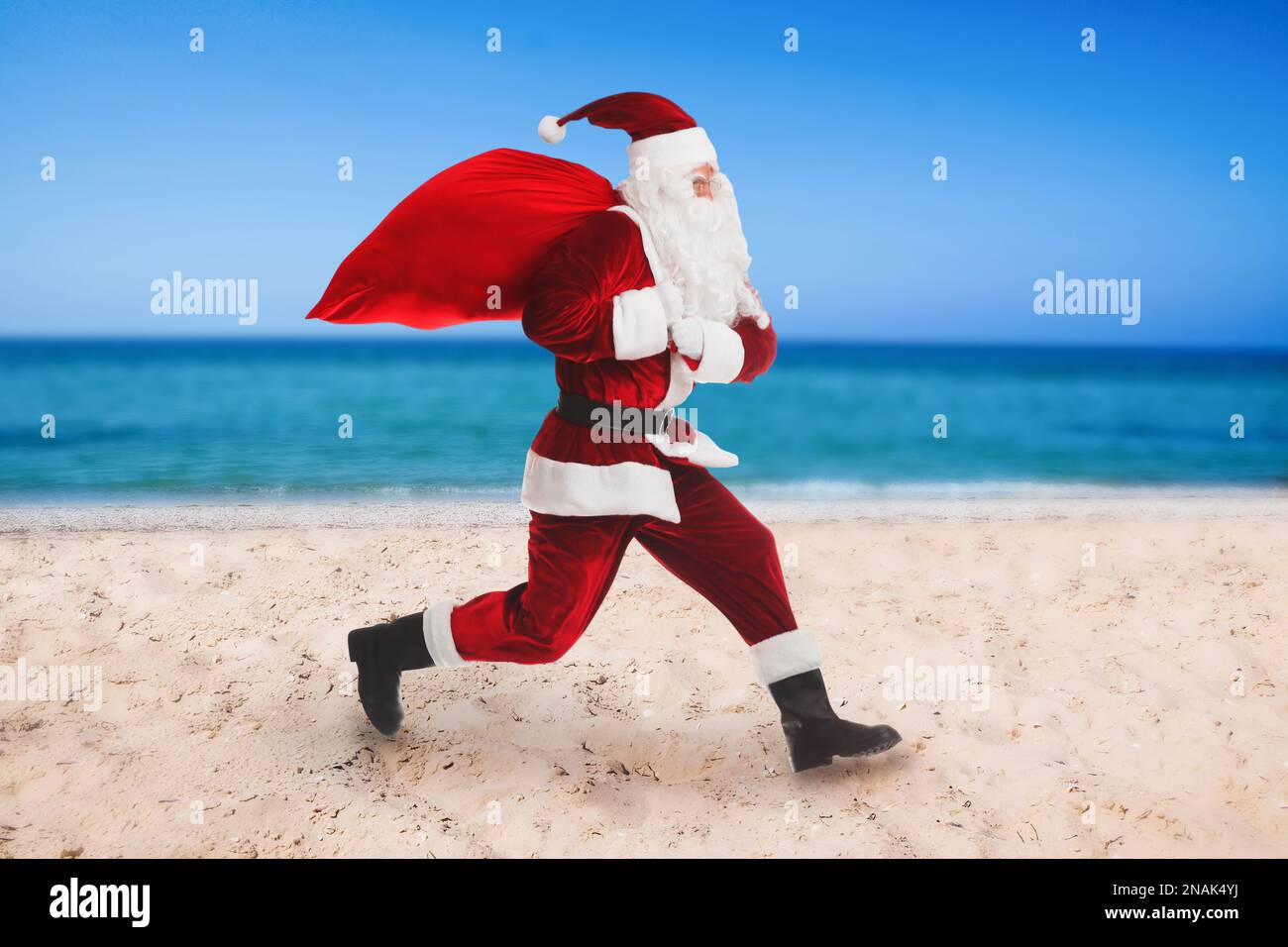 Santa Claus avec sac rouge sur la plage près de la mer. Vacances de Noël Banque D'Images