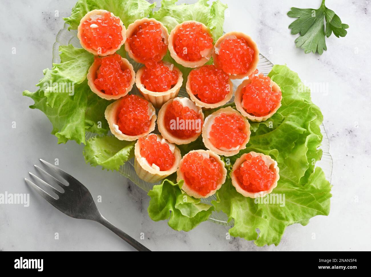 Tartelettes au beurre et caviar rouge. Assiette avec hors-d'œuvre caviar décorée de feuilles de laitue sur fond clair Banque D'Images