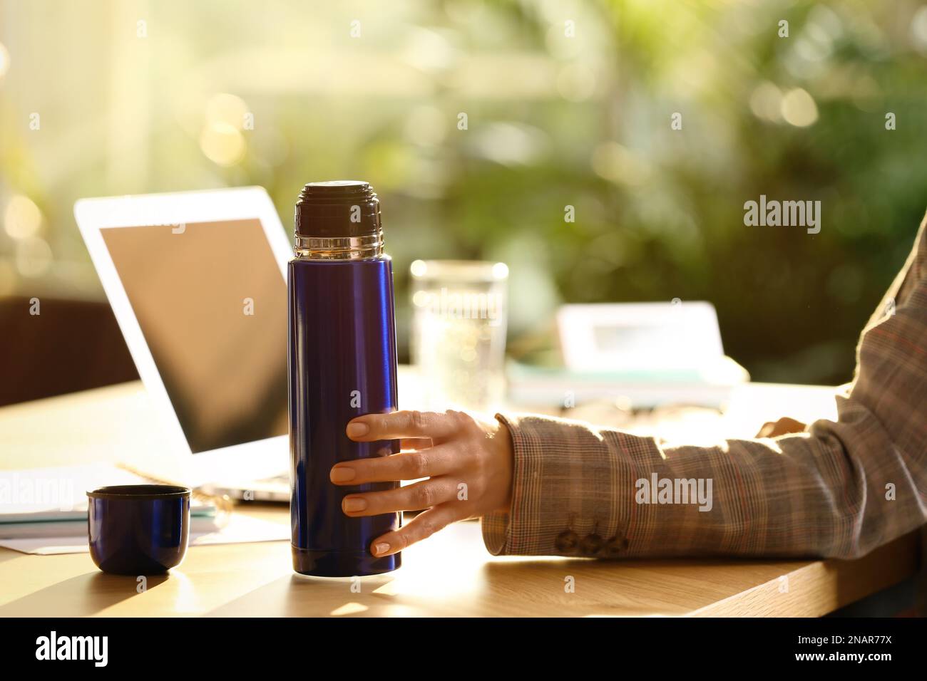 Femme avec bouteille thermos bleue sur le lieu de travail, gros plan Banque D'Images