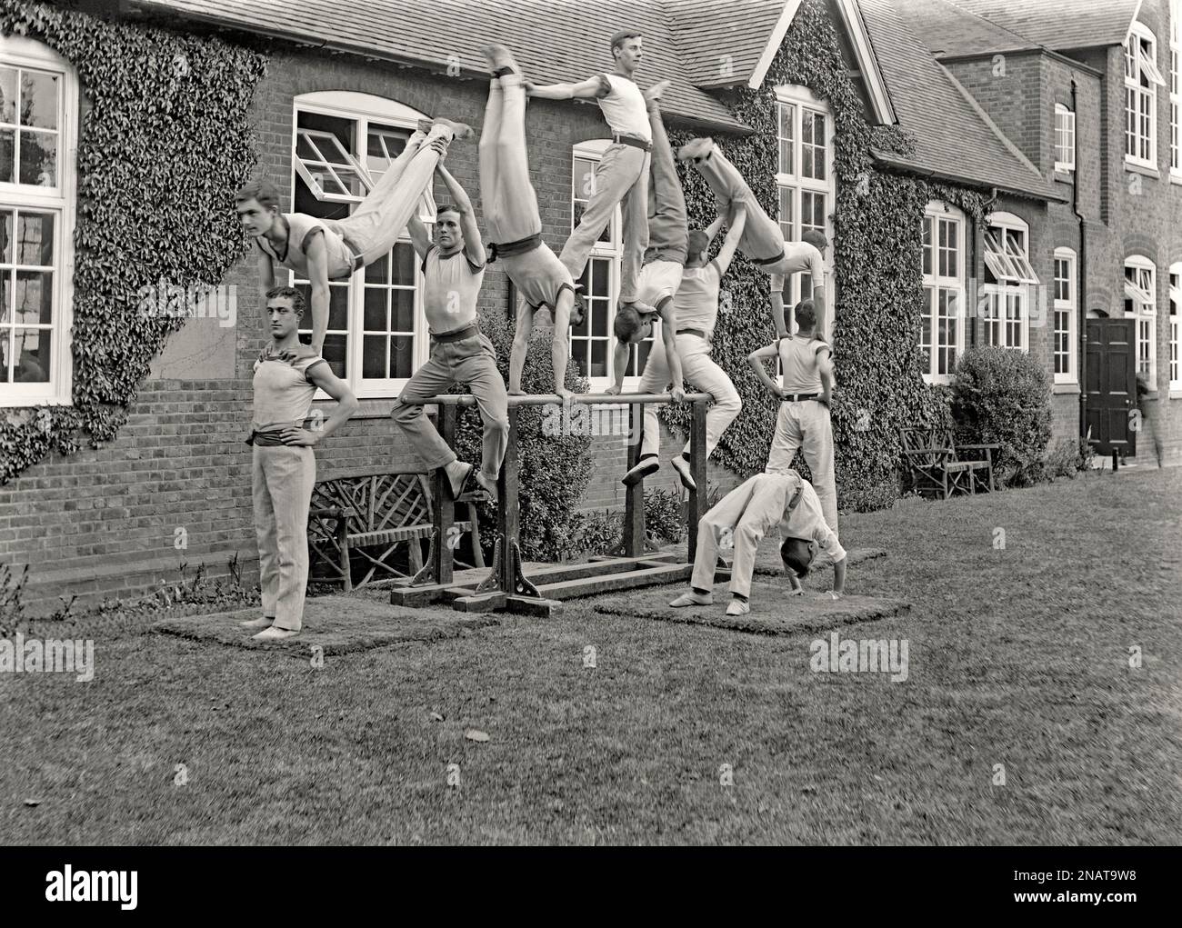 Une exposition de gymnastique en plein air avec 10 hommes posant sur un ensemble de barres parallèles, Royaume-Uni vers 1900. L'équilibre des compétences, de la force, de la forme physique et de la flexibilité sont appelés. L'homme en position haute est soutenu avec ses pieds est sur le cou des deux gymnastes en dessous de lui qui sont en position de la main. Le gymnaste situé à l'avant du groupe est en position de pont. La longue exposition signifie qu'il y a un flou de mouvement causé par le mouvement de certains des hommes tenant la pose – une photographie victorienne/édouardienne vintage 1800s/1900s. Banque D'Images