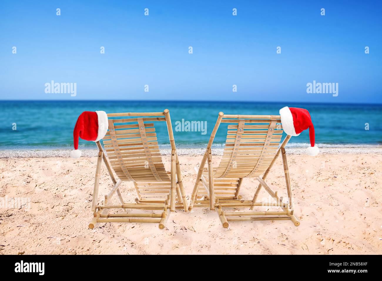 Chaises longues en bois et chapeaux du Père Noël sur la plage près de la mer. Vacances de Noël Banque D'Images