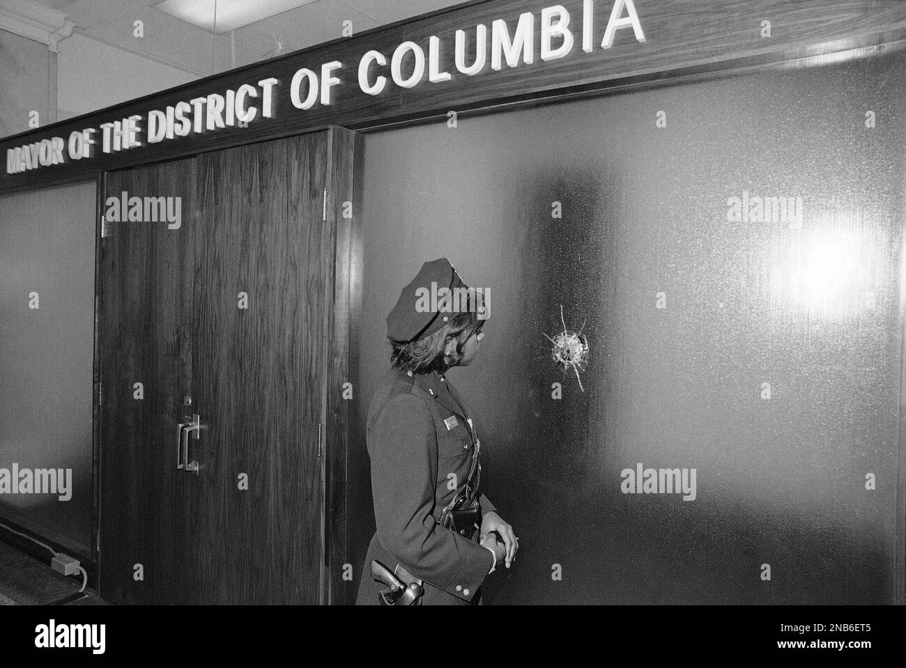 Scene inside the district building in Washington on Friday, March 11, 1977 at the entrance to the mayor’s office. Police officer looks at a bullet hole in the glass. Other signs of gunfire are at left and top of door. (AP Photo) Banque D'Images
