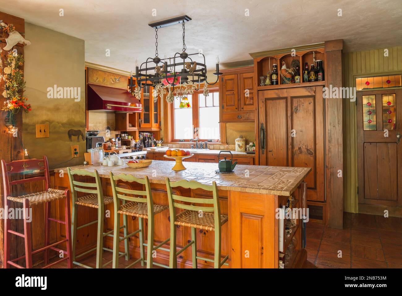 Îlot en bois de pin en pierre et en céramique incrustée avec chaises et armoires en bois et en cuir brut tissé, cuisinière à gaz professionnelle Ultraline dans la cuisine. Banque D'Images