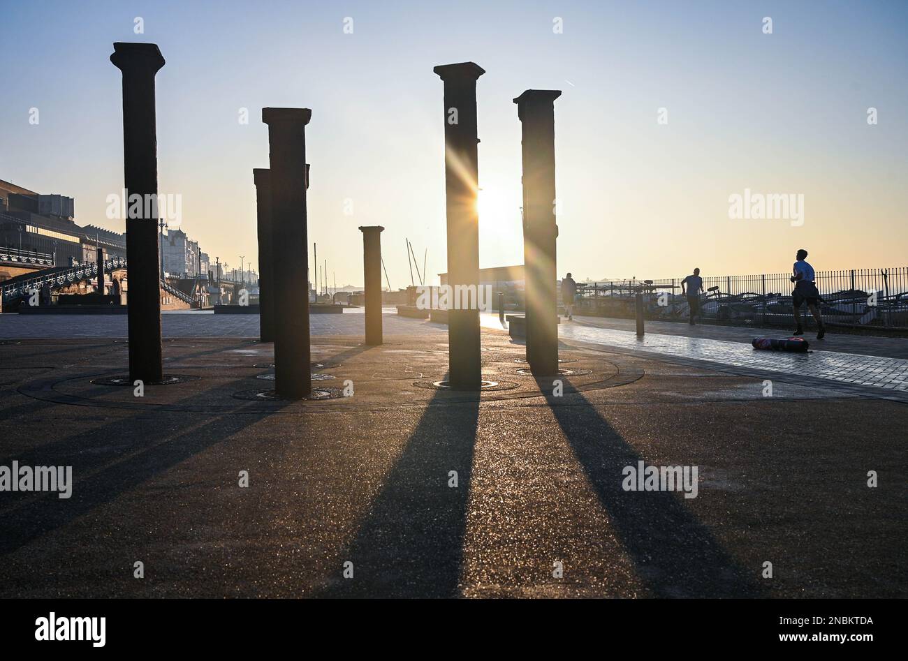 Brighton UK 14th février 2023 - les coureurs passent devant les œuvres d'art Golden Spiral sur le front de mer de Brighton tandis que le soleil se brise dans la brume matinale le long de la côte sud. Il est prévu d'être le jour le plus chaud de l'année jusqu'à présent avec des températures qui devraient atteindre 16 degrés dans certaines parties du Royaume-Uni : crédit Simon Dack / Alamy Live News Banque D'Images