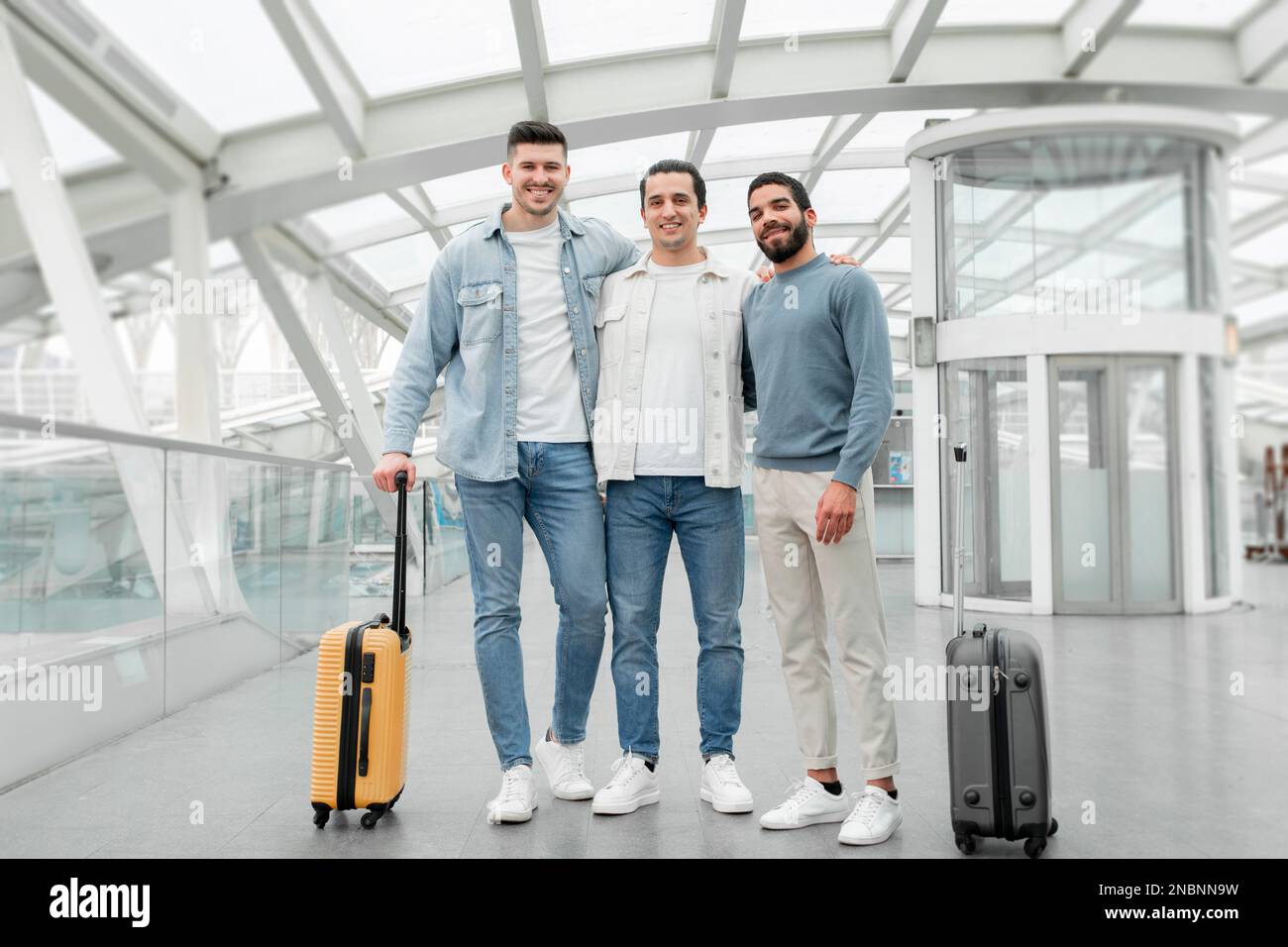 Trois touristes masculins debout avec des valises posant à l'intérieur de l'aéroport Banque D'Images