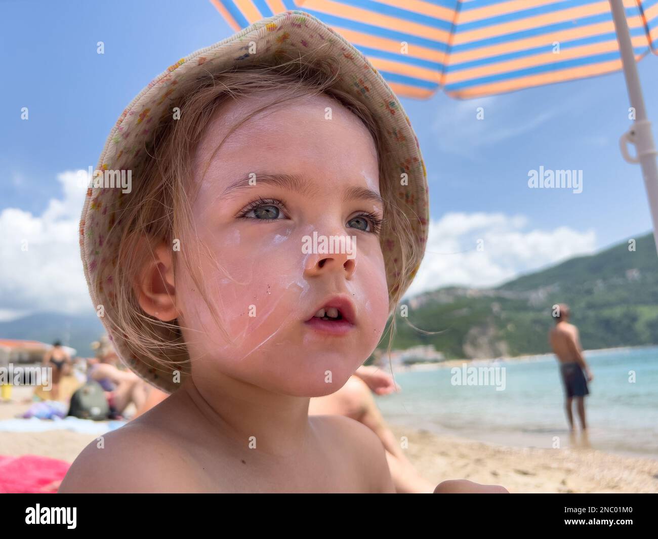 Une petite fille avec de la crème solaire sur son visage est assise sur la  plage sous un parasol Photo Stock - Alamy