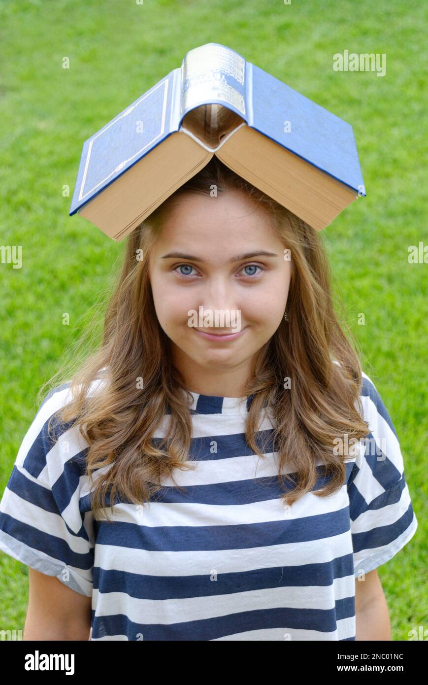 Jeune belle femme avec un grand livre sur sa tête sur le fond d'une pelouse verte Banque D'Images