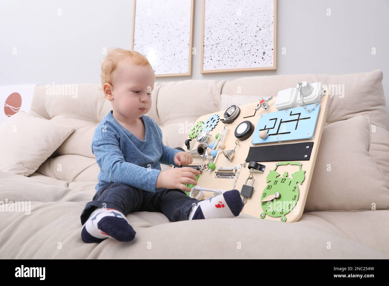 Un petit garçon mignon jouant avec un plateau occupé sur le canapé à la maison Banque D'Images