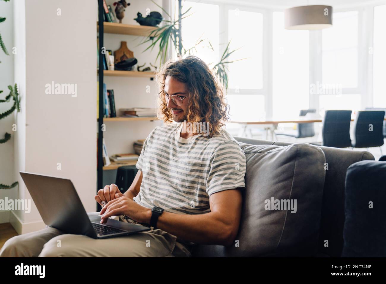 Jeune homme mausseur dans des lunettes souriant et utilisant un ordinateur portable tout en étant assis dans le hall du bureau Banque D'Images